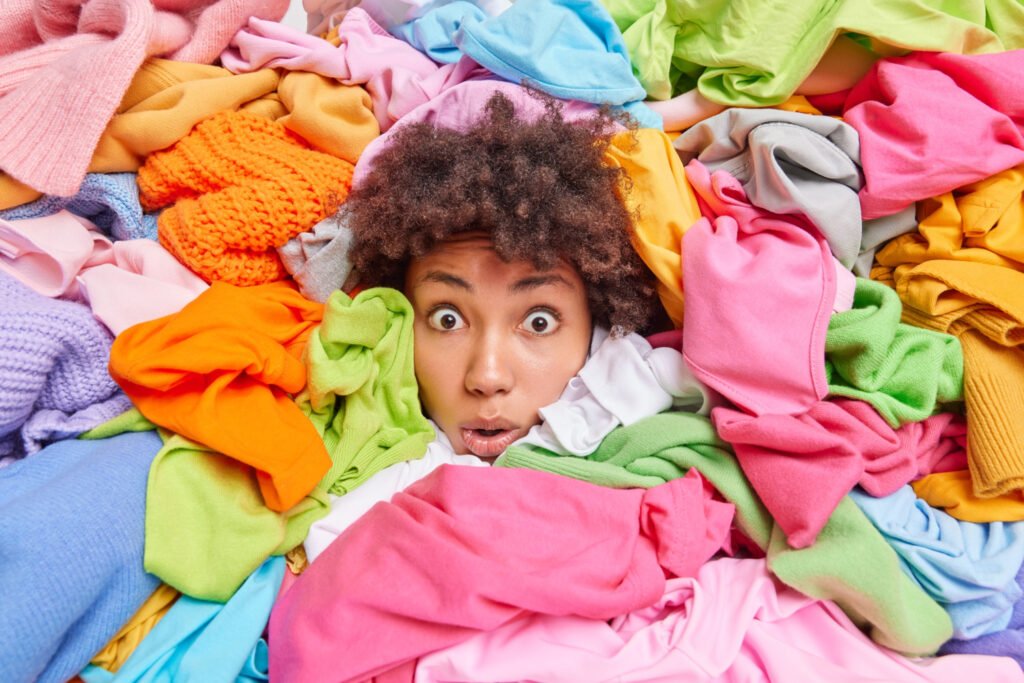 Overwhelmed afro american woman gives advice recycle old clothes sticks out head through multicolored clothing surrounded by unwearable items textile recycling